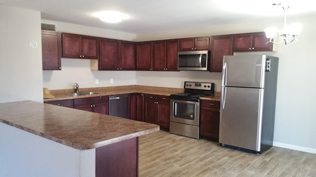 kitchen featuring appliances with stainless steel finishes, a peninsula, light wood-type flooring, a sink, and reddish brown cabinets