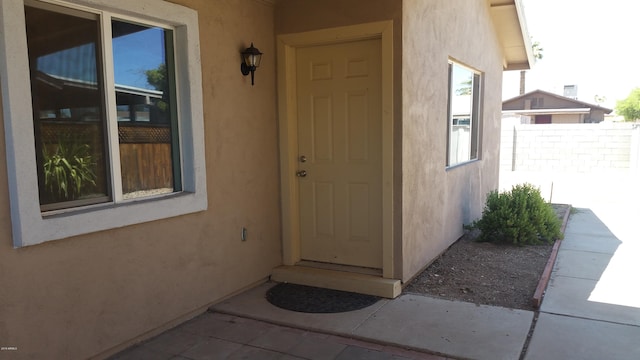 entrance to property featuring stucco siding and fence