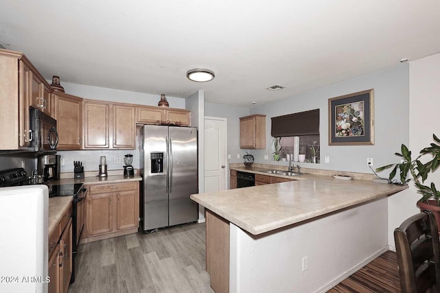 kitchen featuring visible vents, light wood-type flooring, black appliances, a sink, and a peninsula