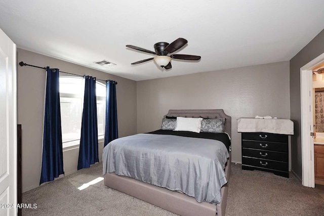 carpeted bedroom with visible vents, ensuite bath, and a ceiling fan