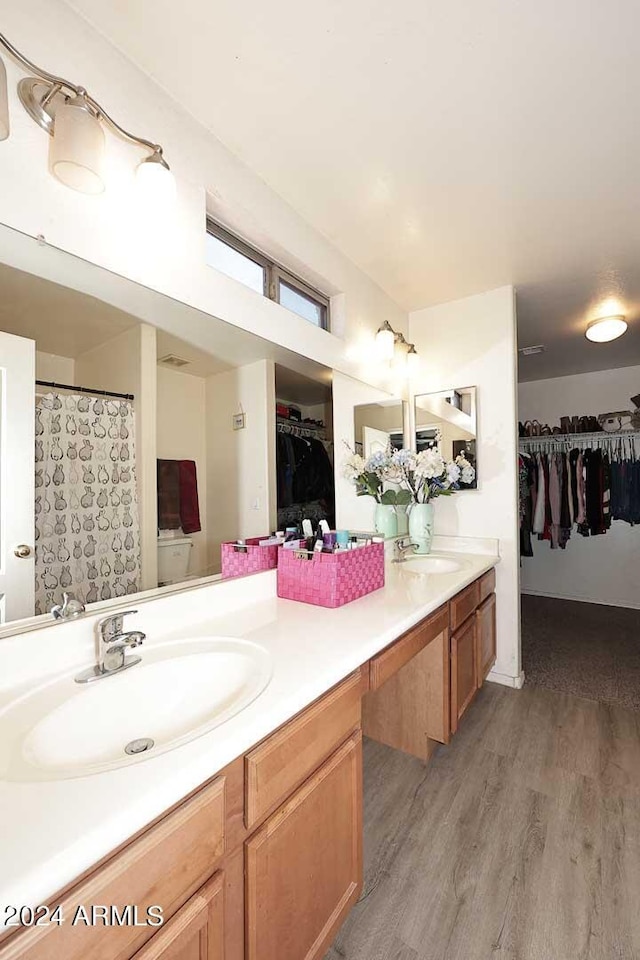 full bathroom with double vanity, a spacious closet, wood finished floors, and a sink