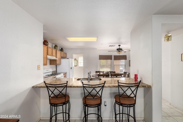 kitchen featuring a breakfast bar area, under cabinet range hood, a peninsula, white appliances, and a sink