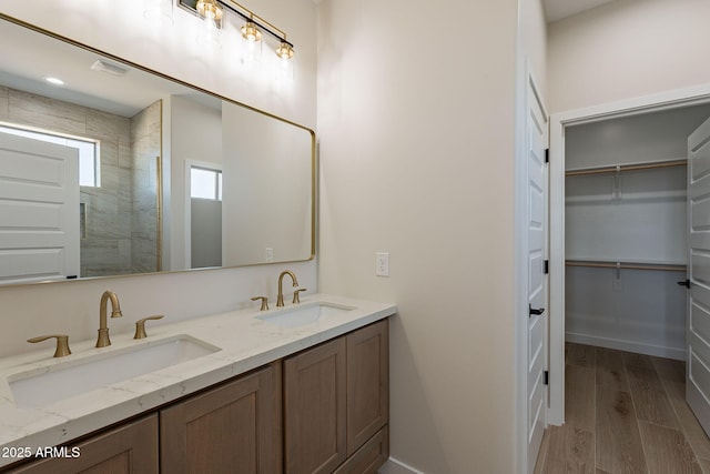 full bathroom with double vanity, wood finished floors, a spacious closet, and a sink