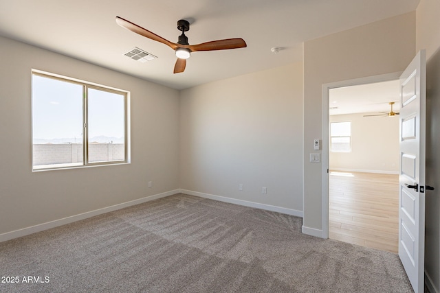 carpeted spare room featuring baseboards, visible vents, and a ceiling fan