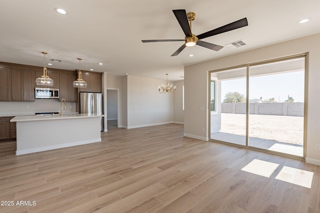 unfurnished living room with ceiling fan with notable chandelier, light wood-type flooring, a sink, and recessed lighting