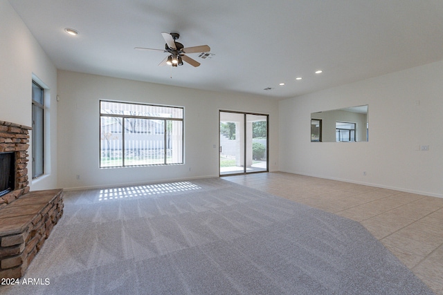 unfurnished living room with ceiling fan, a stone fireplace, light tile patterned floors, and a wealth of natural light