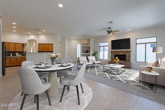 dining space featuring a stone fireplace, light tile patterned floors, and ceiling fan