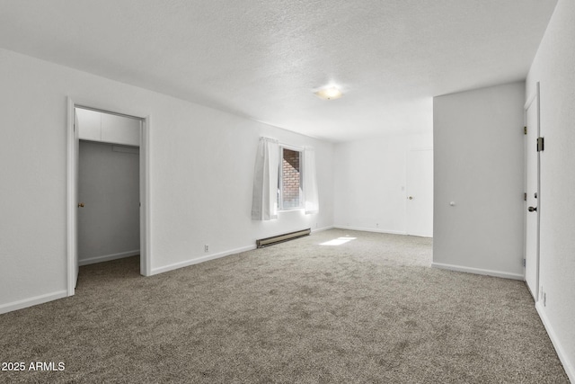 unfurnished bedroom featuring a baseboard heating unit, a walk in closet, a textured ceiling, and carpet