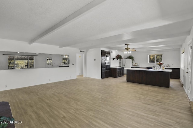 kitchen with light wood-type flooring, beam ceiling, dark brown cabinets, and a kitchen island