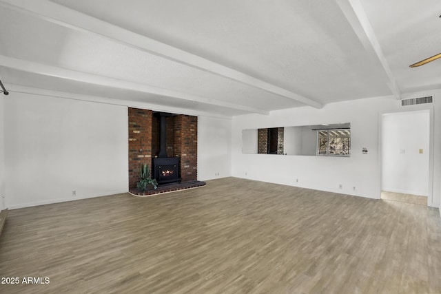 unfurnished living room with beamed ceiling, wood-type flooring, and a wood stove