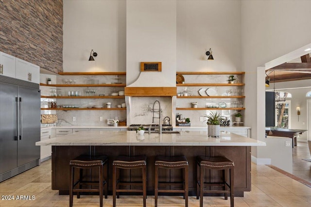 kitchen with built in refrigerator, a breakfast bar, white cabinetry, and a high ceiling