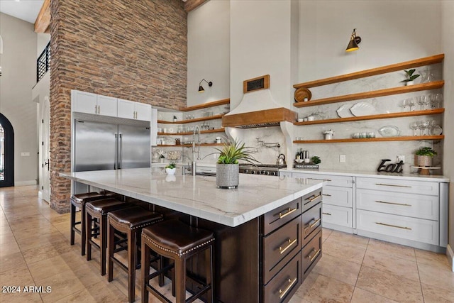 kitchen featuring backsplash, a high ceiling, white cabinets, light stone counters, and a kitchen island with sink