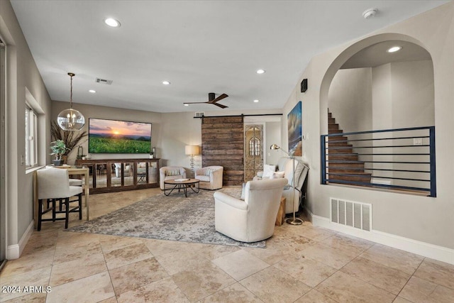 living room featuring a barn door and ceiling fan with notable chandelier