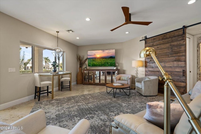 living room with ceiling fan with notable chandelier and a barn door