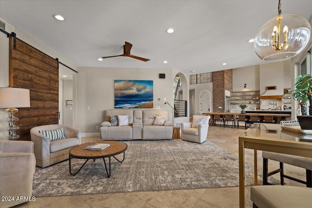 living room with ceiling fan with notable chandelier, light tile patterned floors, and a barn door