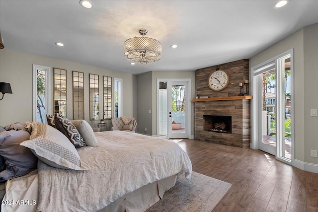 bedroom featuring an inviting chandelier, access to exterior, a large fireplace, and hardwood / wood-style flooring