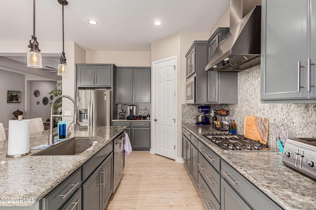 kitchen featuring wall chimney exhaust hood, sink, light stone counters, appliances with stainless steel finishes, and pendant lighting