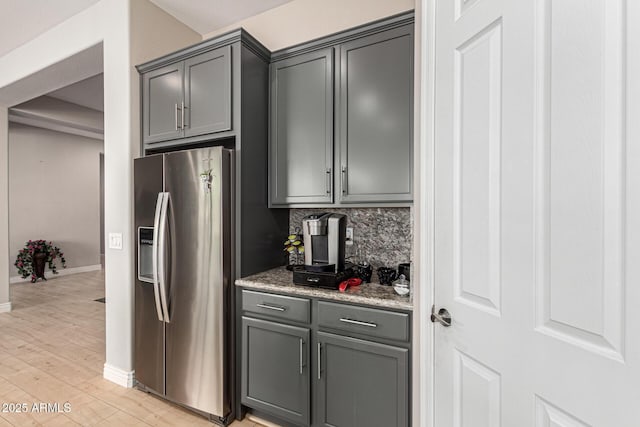 kitchen featuring gray cabinets, backsplash, light stone counters, light hardwood / wood-style floors, and stainless steel fridge with ice dispenser