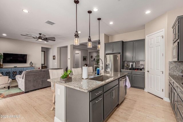 kitchen with sink, decorative backsplash, stainless steel appliances, and a center island with sink