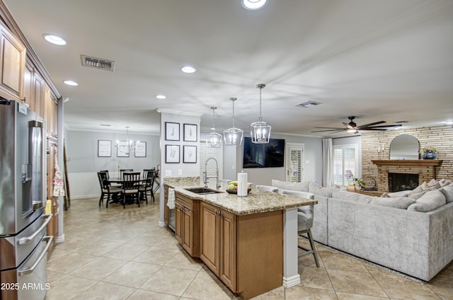 kitchen featuring stainless steel appliances, sink, a center island with sink, a fireplace, and hanging light fixtures