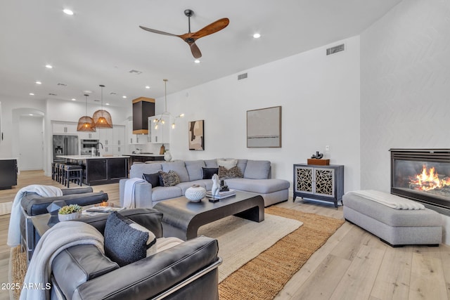 living room featuring arched walkways, light wood finished floors, a premium fireplace, and visible vents