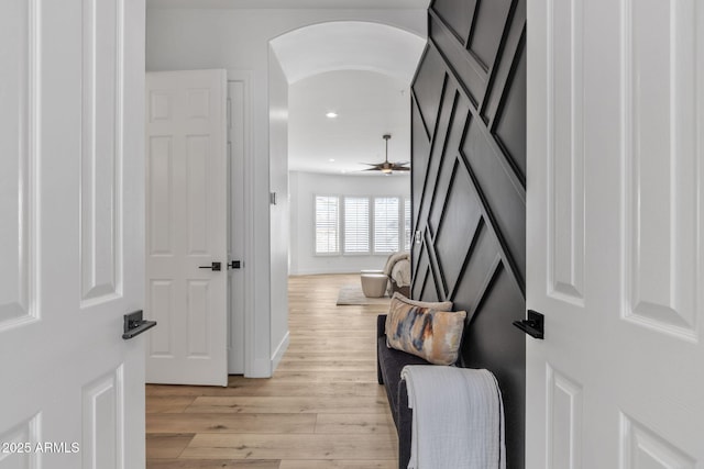 hallway with light wood-style floors, arched walkways, baseboards, and recessed lighting