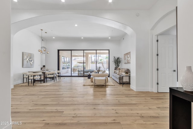 interior space featuring arched walkways, light wood-type flooring, and baseboards