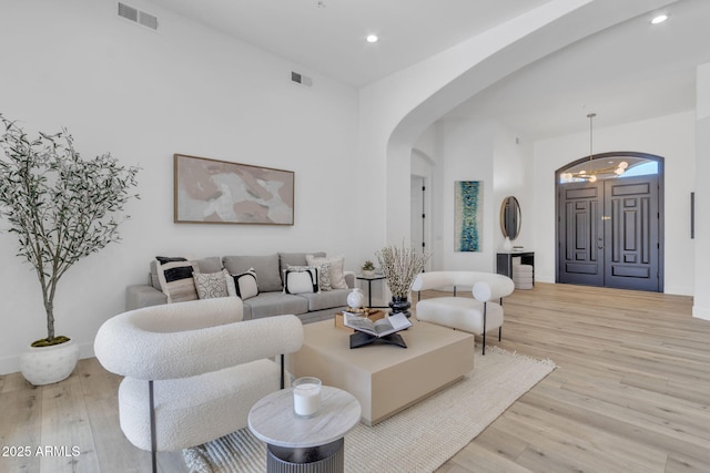 living area with light wood-style floors, visible vents, arched walkways, and recessed lighting