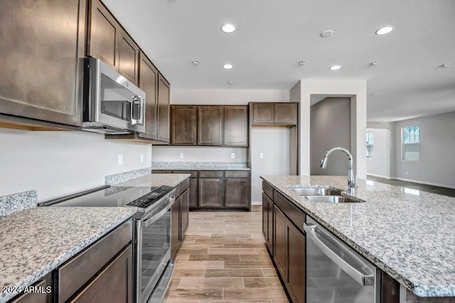 kitchen featuring light stone counters, appliances with stainless steel finishes, dark brown cabinets, sink, and light hardwood / wood-style flooring