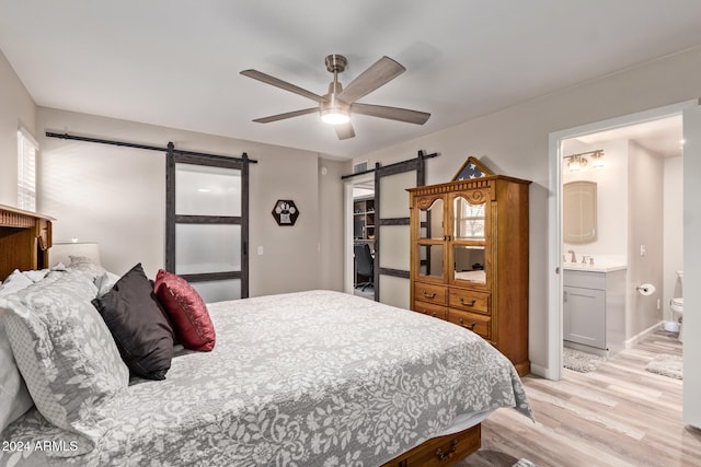 bedroom featuring ceiling fan, a barn door, light wood-type flooring, and ensuite bath