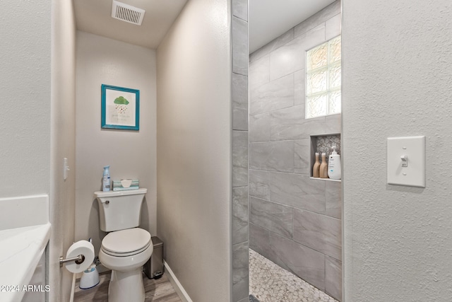 bathroom with tiled shower, hardwood / wood-style flooring, and toilet