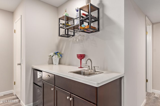 bar with stainless steel fridge, light wood-type flooring, dark brown cabinetry, and sink