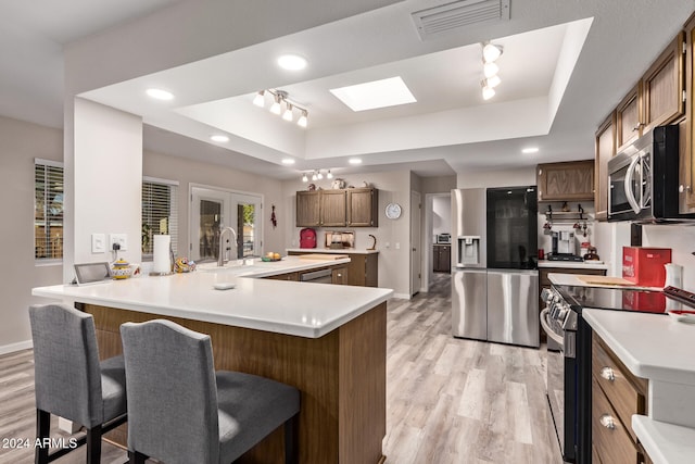 kitchen featuring appliances with stainless steel finishes, a tray ceiling, a kitchen breakfast bar, and light hardwood / wood-style floors