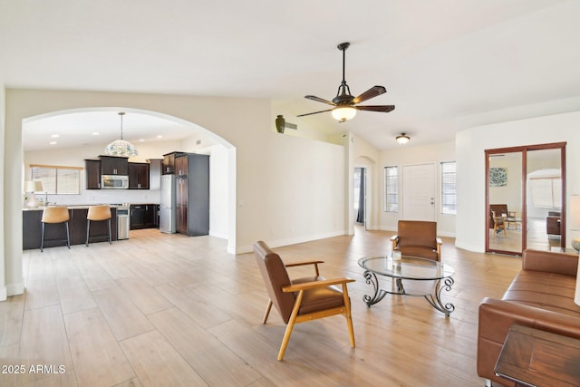 living area with vaulted ceiling, arched walkways, light wood-style flooring, and baseboards