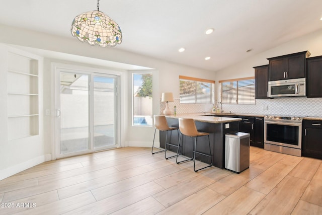 kitchen featuring appliances with stainless steel finishes, a breakfast bar, a healthy amount of sunlight, and hanging light fixtures