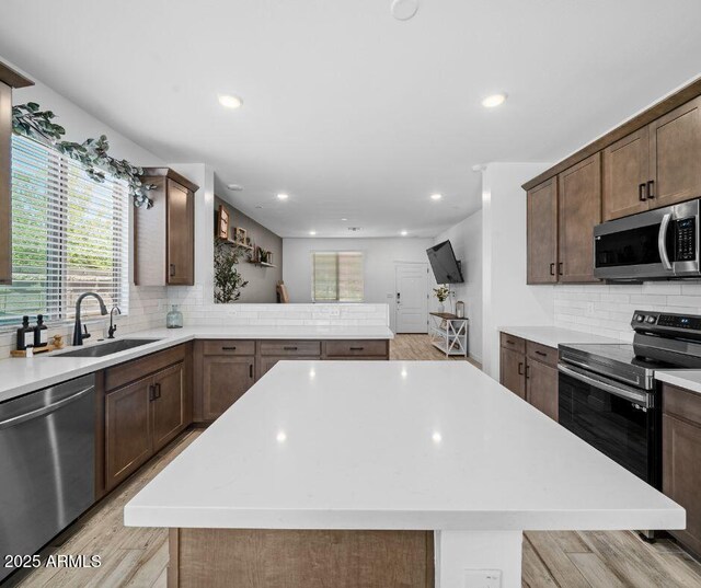 kitchen with backsplash, appliances with stainless steel finishes, a sink, light countertops, and light wood finished floors