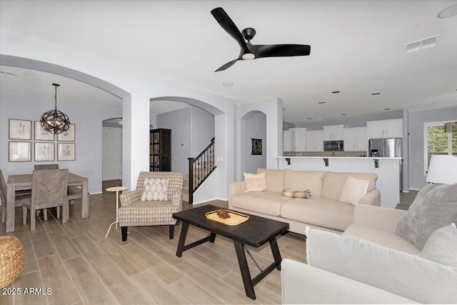 living room featuring ceiling fan with notable chandelier, light wood-style floors, arched walkways, and visible vents