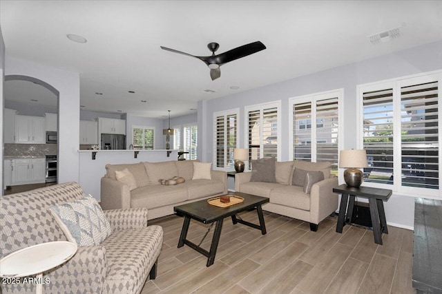 living area featuring arched walkways, a ceiling fan, visible vents, and wood finish floors