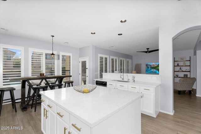 kitchen featuring arched walkways, a kitchen island, light wood-style floors, and a sink