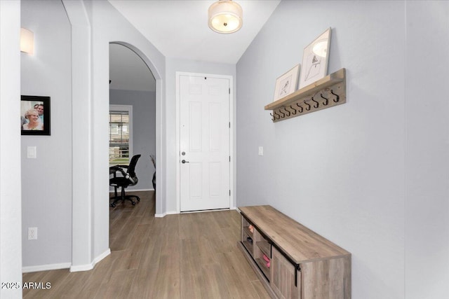 corridor with baseboards, arched walkways, and wood finished floors