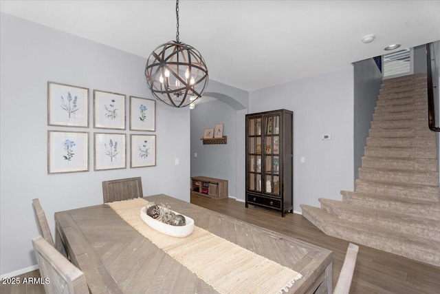 dining space featuring stairs, an inviting chandelier, wood finished floors, and arched walkways