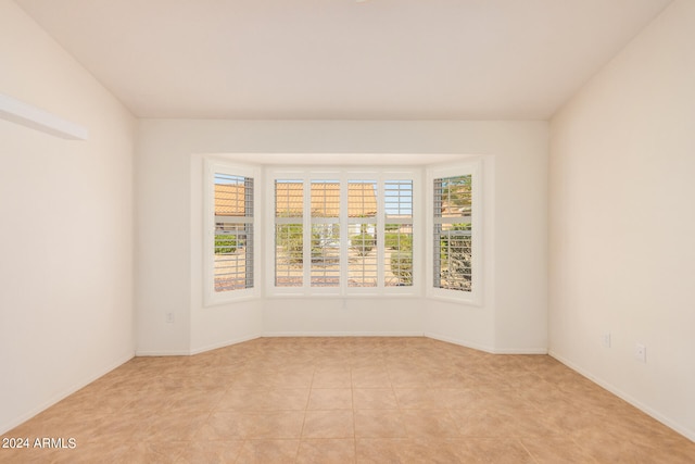 tiled empty room featuring lofted ceiling