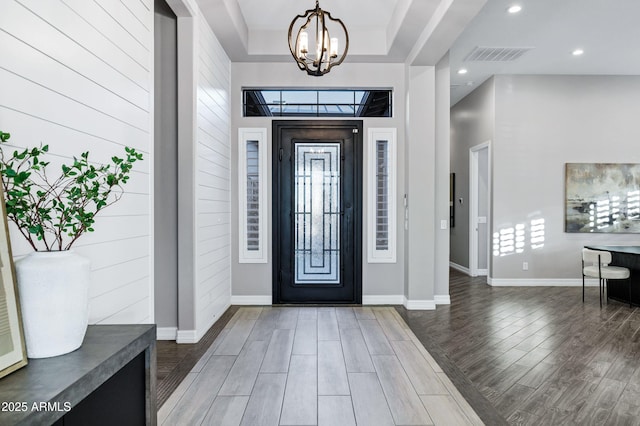 entryway with baseboards, a chandelier, wood finished floors, and visible vents
