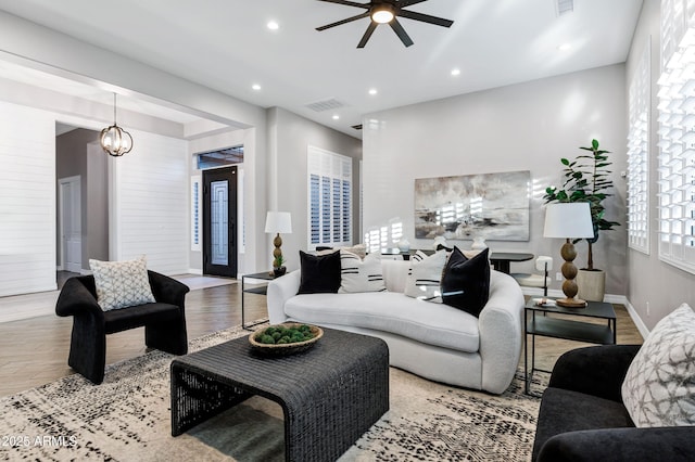 living room with visible vents, baseboards, ceiling fan with notable chandelier, and wood finished floors