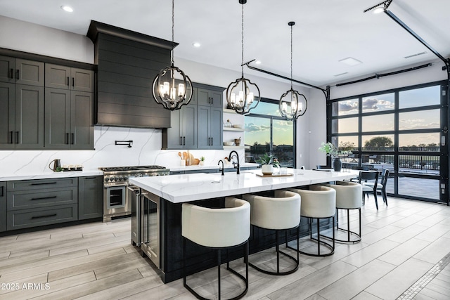 kitchen with light stone counters, a chandelier, double oven range, range hood, and tasteful backsplash