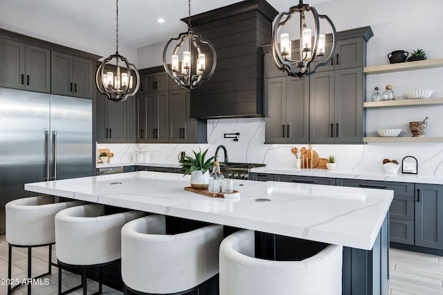 kitchen with open shelves, an inviting chandelier, stainless steel built in fridge, and light stone countertops