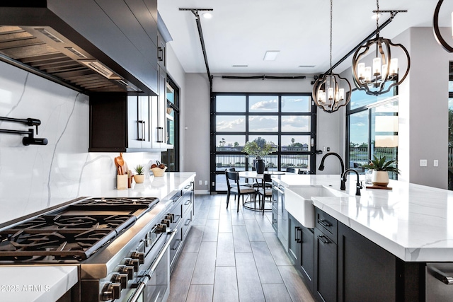 kitchen with light stone countertops, custom range hood, a sink, a notable chandelier, and double oven range