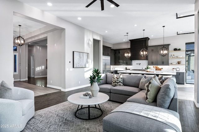 living room with dark wood-style flooring, baseboards, recessed lighting, and ceiling fan with notable chandelier