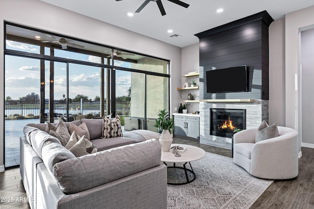 living area featuring a high end fireplace, ceiling fan, wood finished floors, and visible vents