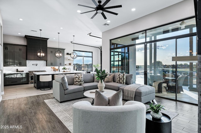 living room featuring recessed lighting, light wood-style floors, and ceiling fan with notable chandelier
